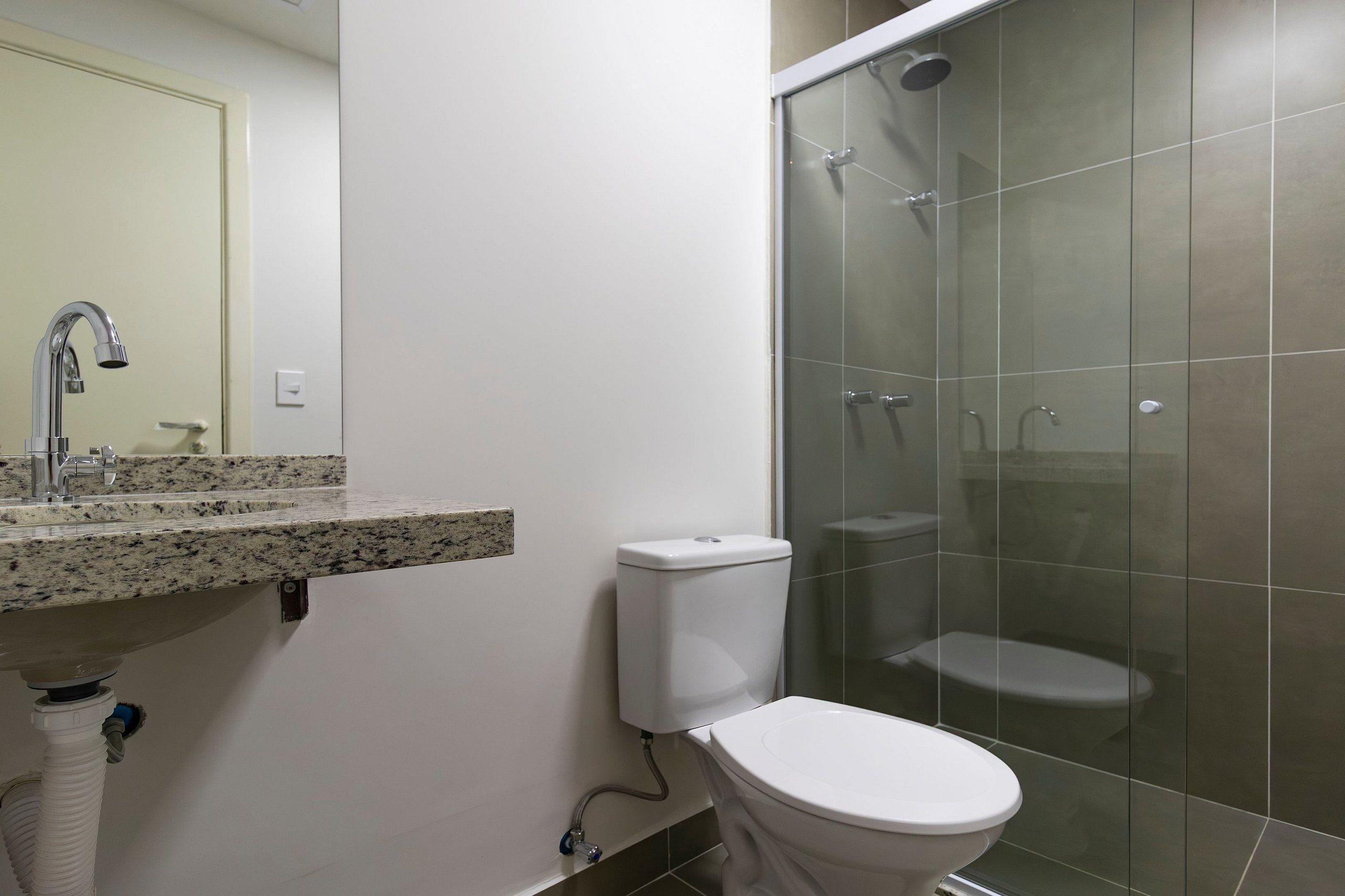 A bathroom with a granite countertop, a white toilet, and a glass-enclosed shower area.