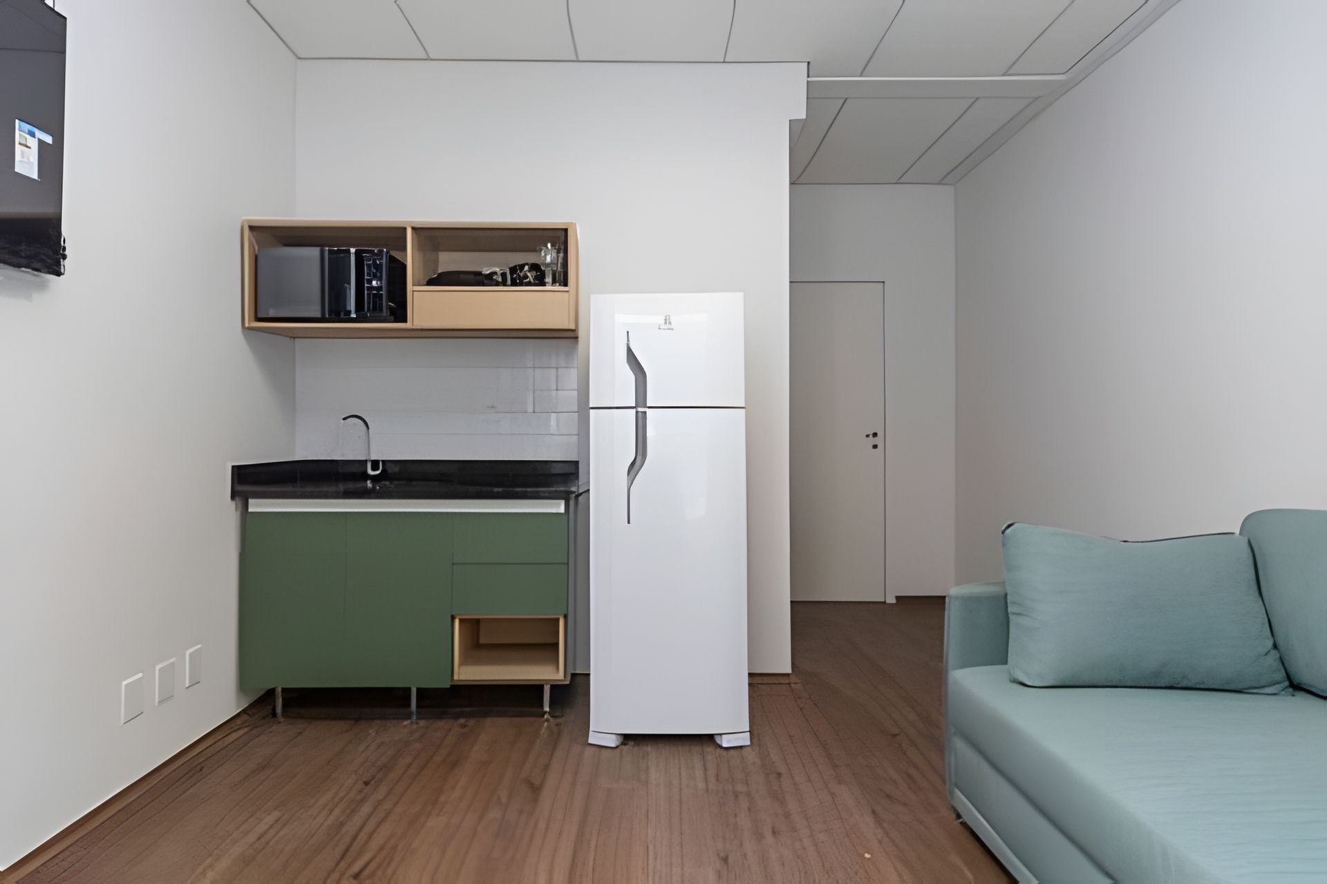A compact kitchen with a refrigerator, a sink, and a wooden shelf above.