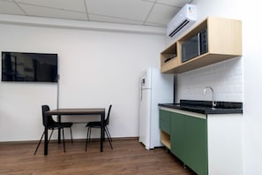 Cozinha compacta com micro-ondas, geladeira, mesa de jantar com cadeiras e TV fixada na parede.