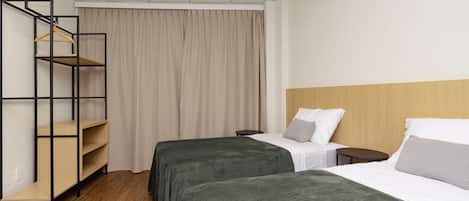 A hotel room with two beds, a wooden headboard, a wardrobe with a hanging rack, and a curtain.