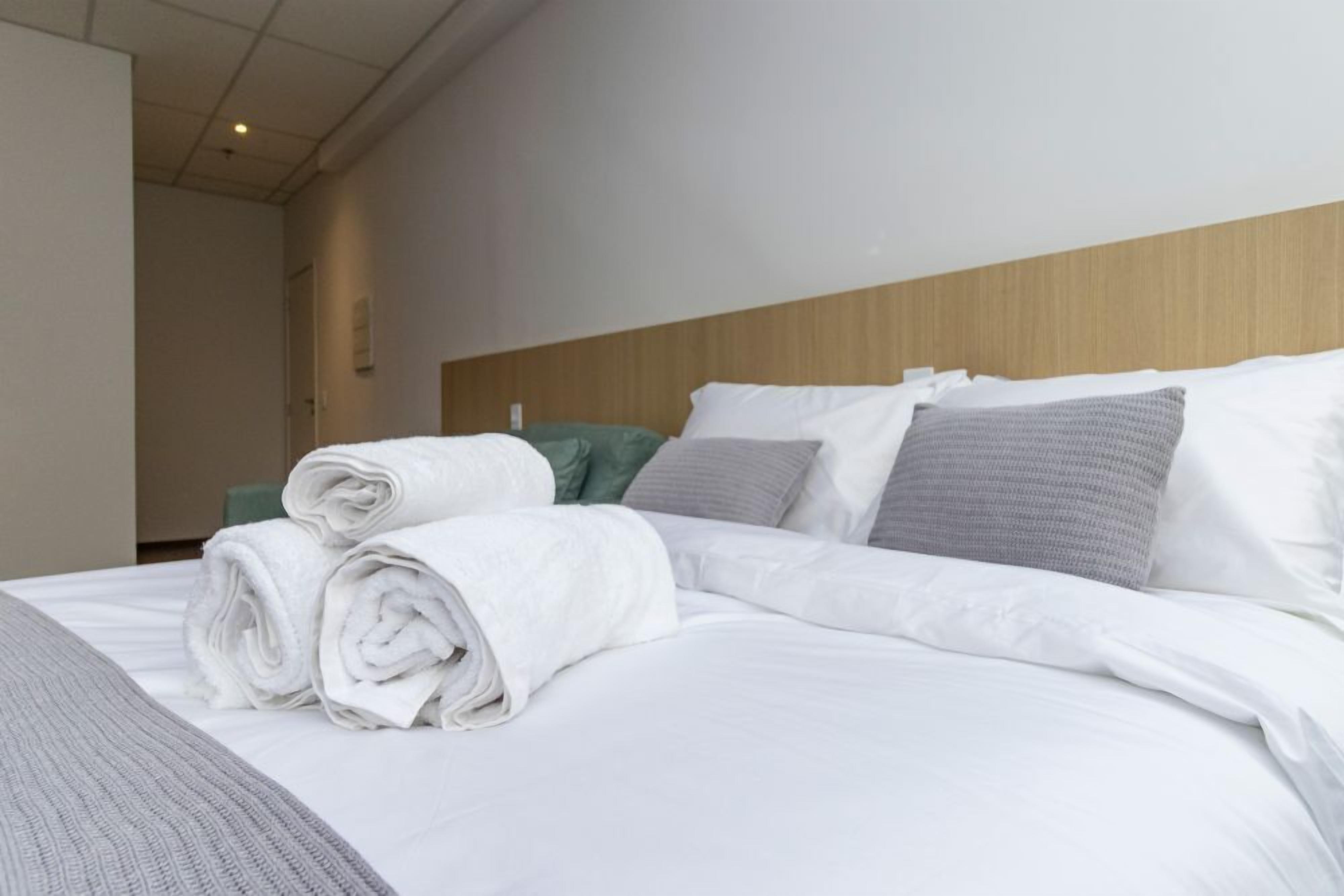 Una camera d'albergo con un letto rifatto, una testiera in legno e vista sul corridoio.