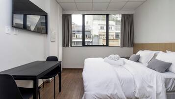 Une chambre d’hôtel comprenant un lit, un bureau, une chaise, un téléviseur fixé au mur et une fenêtre avec des rideaux.