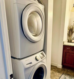 Eine nebeneinander gestellte Waschmaschine und ein Trockner in einem Badezimmer mit einem Holzkabinent und einem Blumenstrauß aus getrockneten Blumen auf der Ablagefläche.