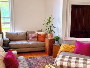 Ein Wohnzimmer mit einer Couch, einem kleinen Tisch mit einer Pflanze, einem gemusterten Teppich und einer Tür im Hintergrund.