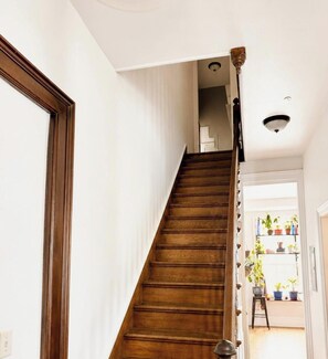 Eine Holztreppe mit Handlauf, weißen Wänden und einer Deckenleuchte.