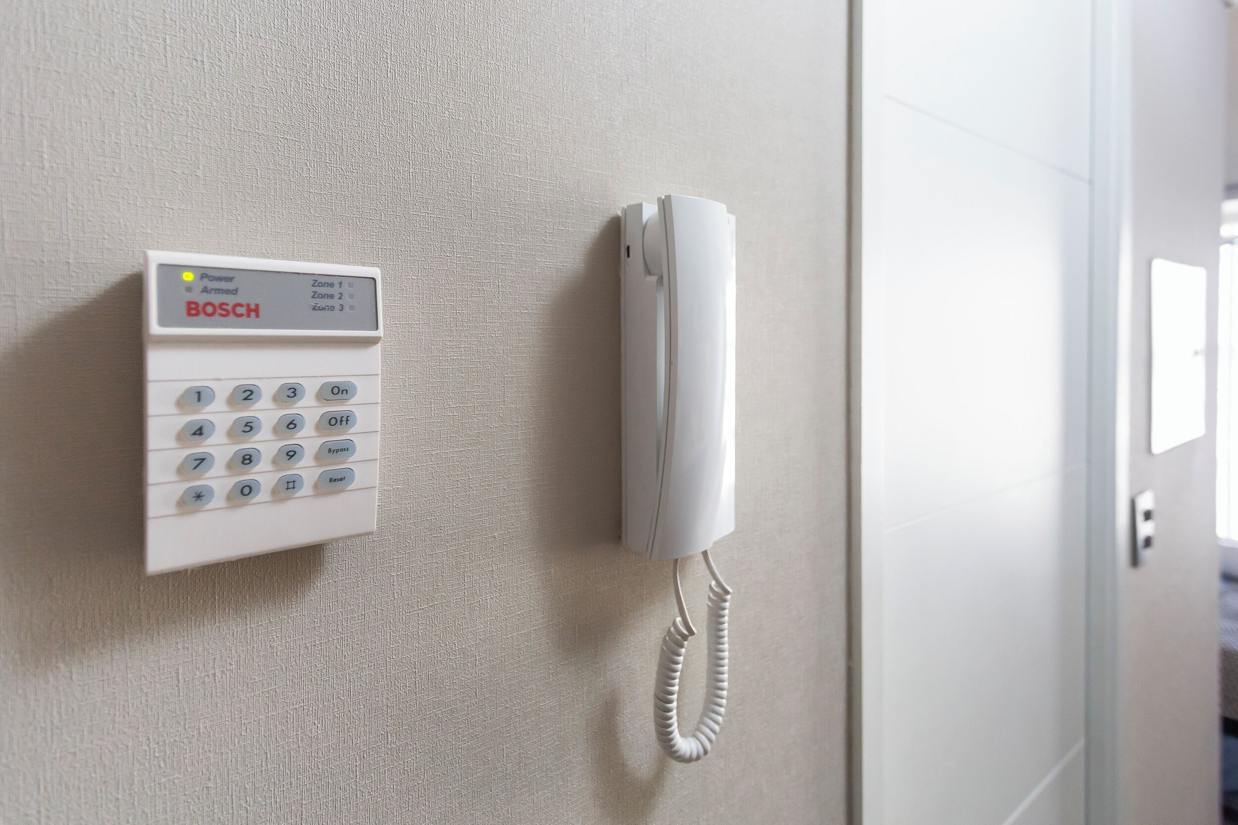 Ein weißes, an der Wand montiertes Telefon mit Zahlenschlüssel und Kabelhandteil.