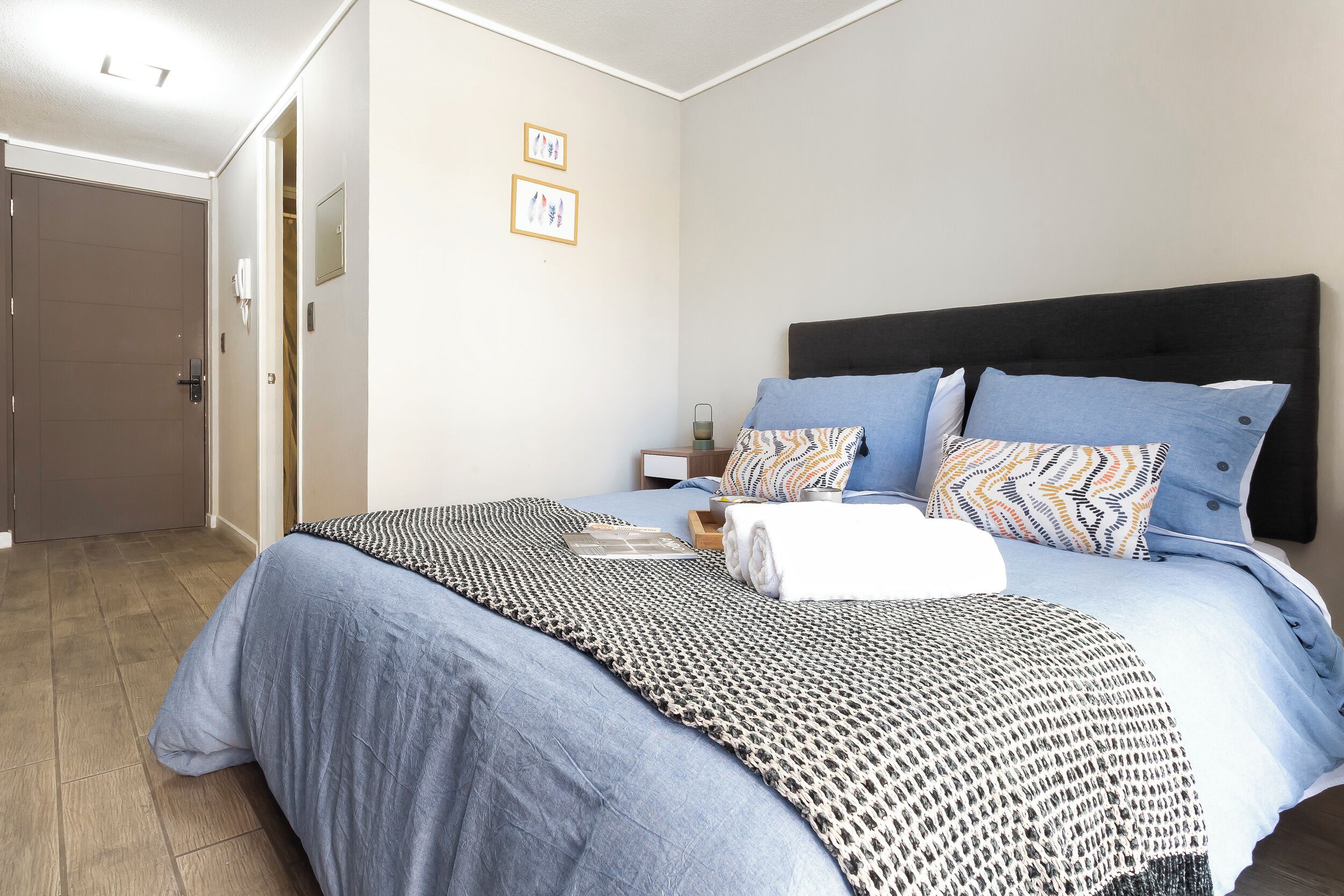 Une chambre à coucher comprenant un lit, une table de chevet, une commode, une porte et un mur orné de deux tableaux encadrés.