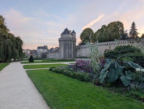 A castle with a tower, surrounded by a well-maintained garden with various plants and a paved walkway. - Au Soleil Levant 2 - PLESCOP (PLESCOP)