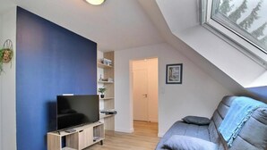 Un salon moderne équipé d’un téléviseur à écran plat, d’un canapé, d’une bibliothèque et d’une porte donnant sur une autre pièce.