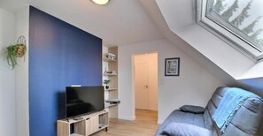 A modern living room with a flat-screen TV, a sofa, a bookshelf, and a door leading to another room. - Au Soleil Levant 2 - PLESCOP (PLESCOP)