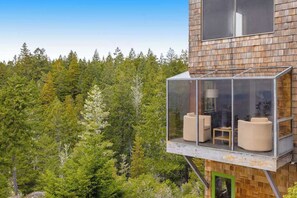 A modern wooden building with a glass balcony featuring two sofas and a table. - Ocean-view main house and private cottage (Gualala)
