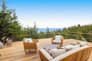 A wooden deck with outdoor furniture, a railing, and a view of the ocean and trees. - Ocean-view main house and private cottage (Gualala)