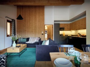 Eine moderne Küche mit Holzausstattung, eine Essecke mit Tisch für Zwei und ein Wohnzimmer mit Sofa und Couchtisch.