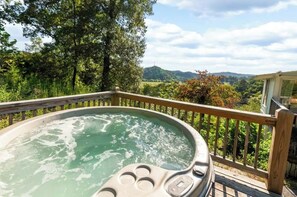 A hot tub on a wooden deck with a view of a forest and hills.