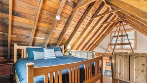A loft bedroom with a wooden ceiling, a bed with blue bedding, a wooden ladder, and a window. - Cozy Mountain Retreat w/ Hot Tub, Fire Pit & Views (Sevierville)