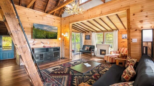 A wooden cabin interior with a fireplace, a sofa, a coffee table, and a television. - Cozy Mountain Retreat w/ Hot Tub, Fire Pit & Views (Sevierville)