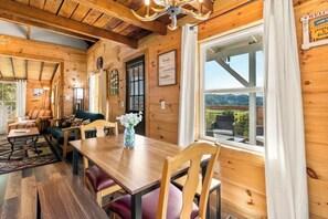 A wooden interior with a dining table, chairs, a sofa, and a chandelier.