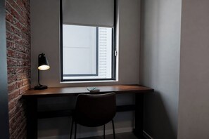 Ein Schreibtisch mit Stuhl, Lampe und Fenster mit Jalousien.