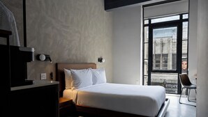 A modern bedroom with a bed, bedside tables, a desk, and a chair. - Sosuite | City View Queen Room w Desk (Philadelphia)