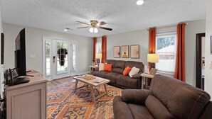 A living room with a ceiling fan, a sofa, a coffee table, and a television. - Relaxing 2BR 1BA Townhome • Loaded Amenities • Central Location Near I-40 (Jackson)
