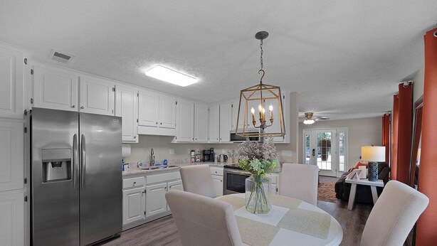 A modern kitchen with white cabinets, a stainless steel refrigerator, a dining table with chairs, and a hanging light fixture. - Relaxing 2BR 1BA Townhome • Loaded Amenities • Central Location Near I-40 (Jackson)