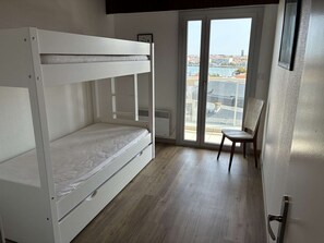 A room with a bunk bed, a chair, and a view of a marina through a glass door. - Evasion Marina Saint Gilles Croix de Vie (SAINT GILLES CROIX DE VIE)