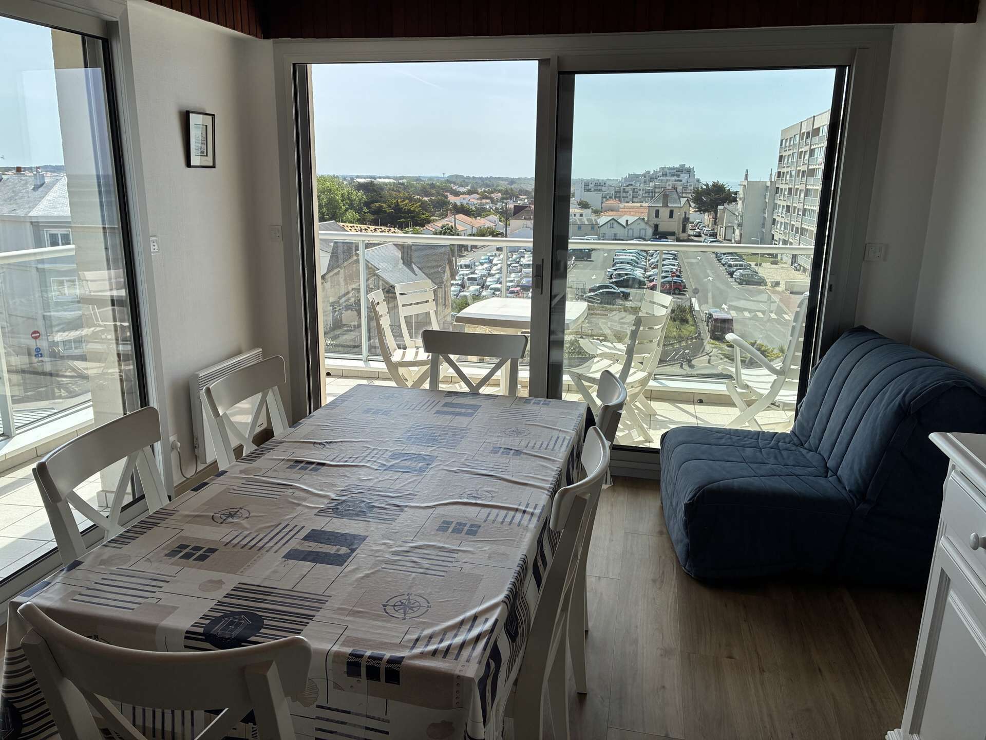 En balkong med ett bord täckt av en karta, en blå soffa och utsikt över en stadspanorama.