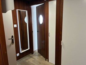 Ein Korridor mit Holzwänden, einem Spiegel und einer Tür mit rundem Fenster.