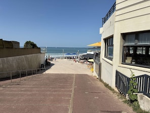 Ein Küstenweg, der zu einem Strand mit Außenbestuhlung und Meerblick führt.