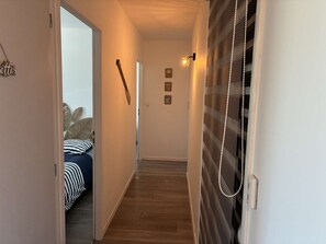 A hallway with a bed, a wall-mounted light, and a door with a curtain. - Villa Marthe Océane - Bretignolles sur mer (BRETIGNOLLES SUR MER)