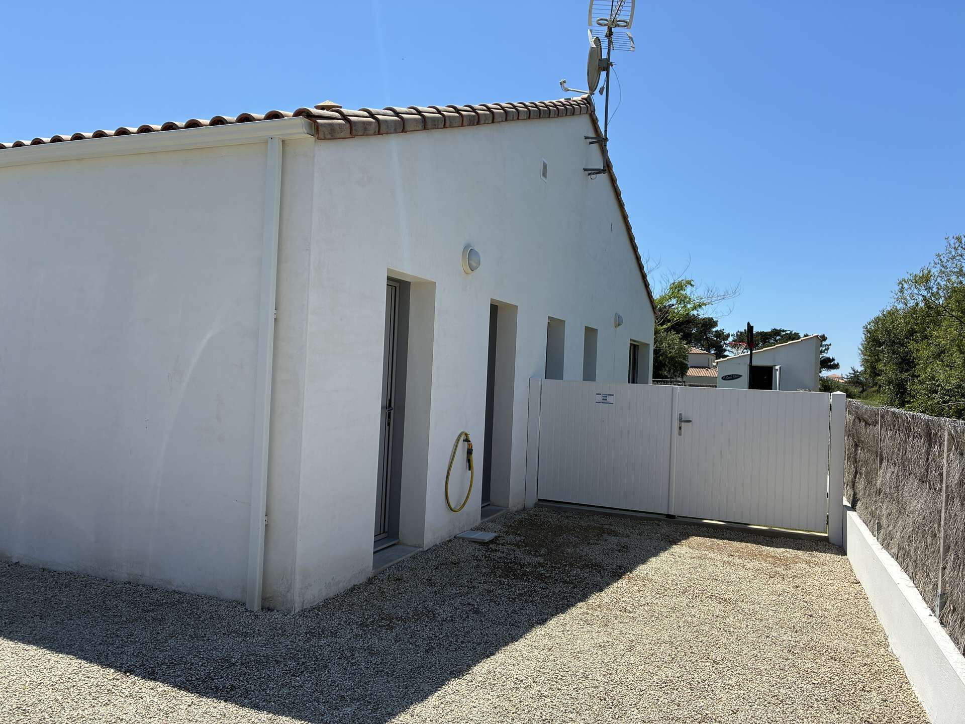 A white building with a tiled roof, a gravel driveway, and a white fence.