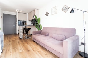 A modern living room with a sofa, a coffee table, a plant, and a kitchen in the background.