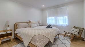 Ein Schlafzimmer mit einem Bett, Nachttischen, einem Sessel und einem Fenster mit Vorhängen.
