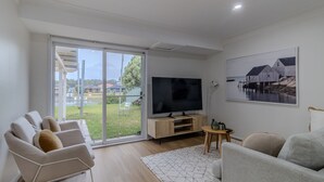 Ein modernes Wohnzimmer mit Fernseher, bequemen Sitzmöglichkeiten, einem großen Fenster und einem Bild an der Wand.