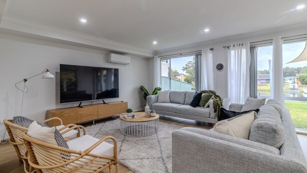 Ein modernes Wohnzimmer mit Flachbildfernseher, grauen Sofas, einem Couchtisch und einem großen Fenster mit Vorhängen.