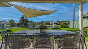 Alpendre coberto com mesa e cadeiras, um vaso de planta e vista para um lago e casas.