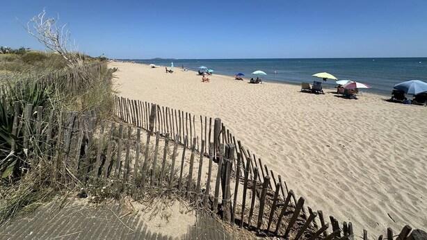 Une plage de sable avec une clôture en bois, des parasols et des chaises de plage.