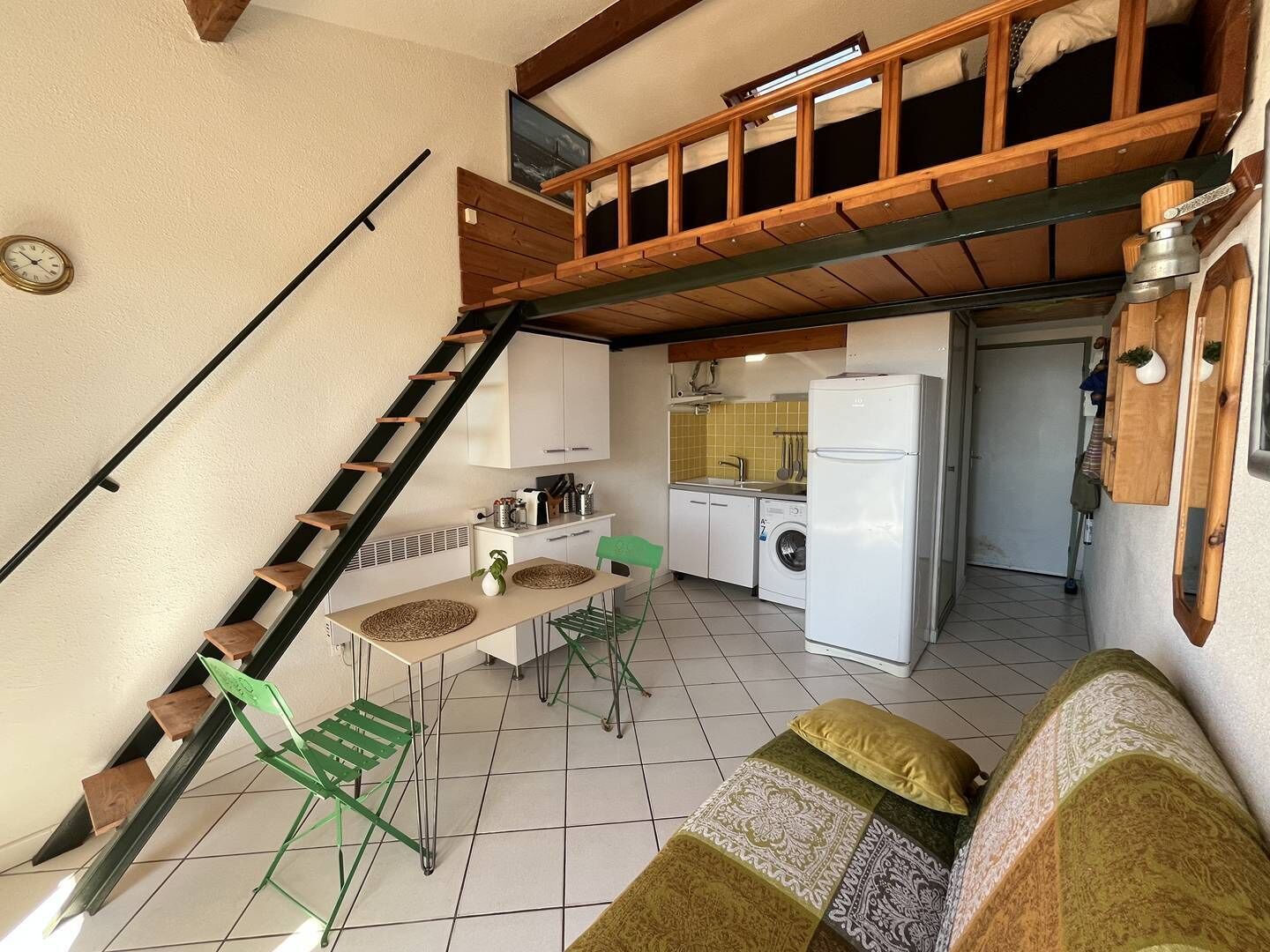 A compact kitchen with a washing machine, a dining area with a table and chairs, and a staircase leading to an upper level.