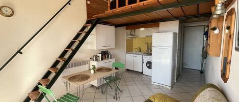A compact kitchen with a washing machine, a dining area with a table and chairs, and a staircase leading to an upper level.