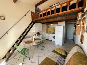 Eine kompakte Küche mit Waschmaschine, eine Essecke mit Tisch und Stühlen sowie eine Treppe, die in ein Obergeschoss führt.