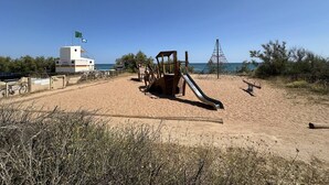 Une plage avec une tour de surveillance pour les sauveteurs, une structure de jeux en bois et un ciel bleu dégagé.