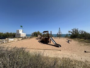 Ein Strand mit einem Rettungsturm, einer Holzspielanlage und einem wolkenlosen, blauen Himmel.