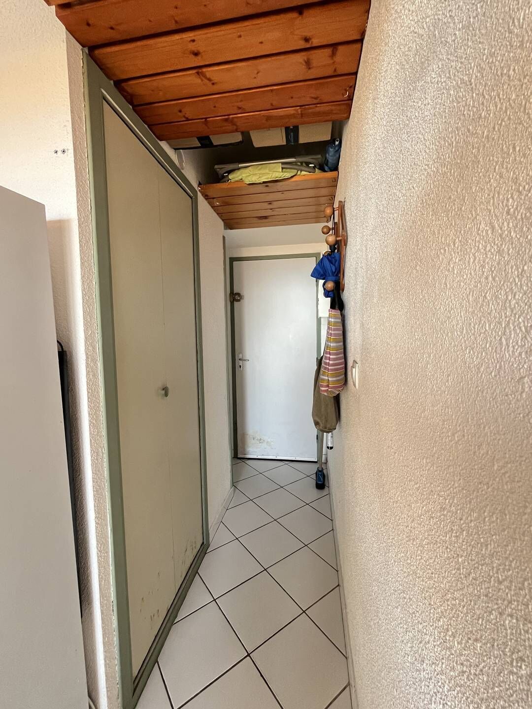 En smal hall med ett kaklat golv, ett träpanelat tak och en dörr längst ner.