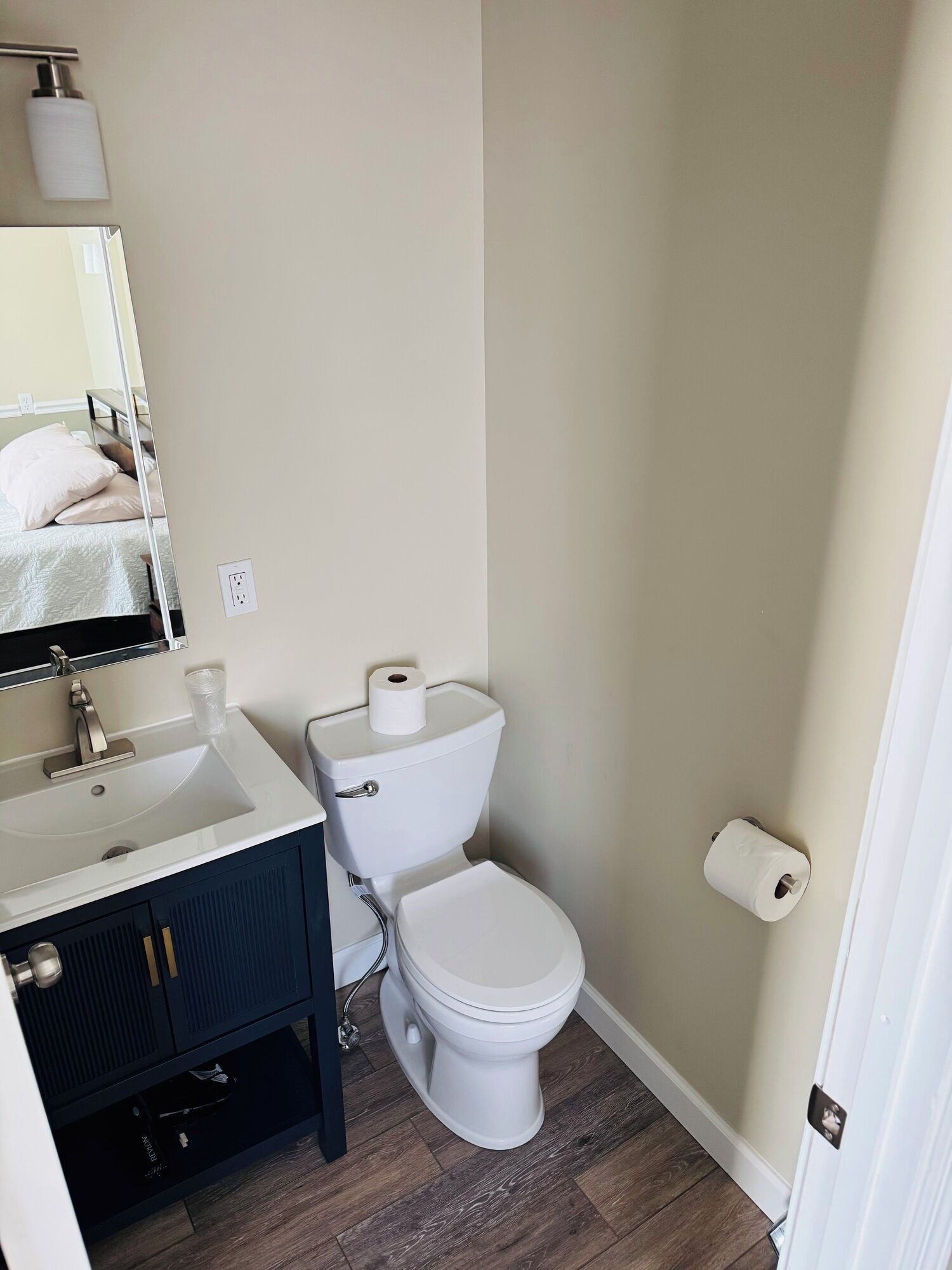 A bathroom with a white sink, dark cabinets, a toilet, and a mirror.