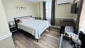 A bedroom with a bed, bedside tables, an air conditioning unit, a TV, and a desk with a chair. - Nestle Inn is a charming, historic hotel located in the heart of Hermann, MO (Hermann)