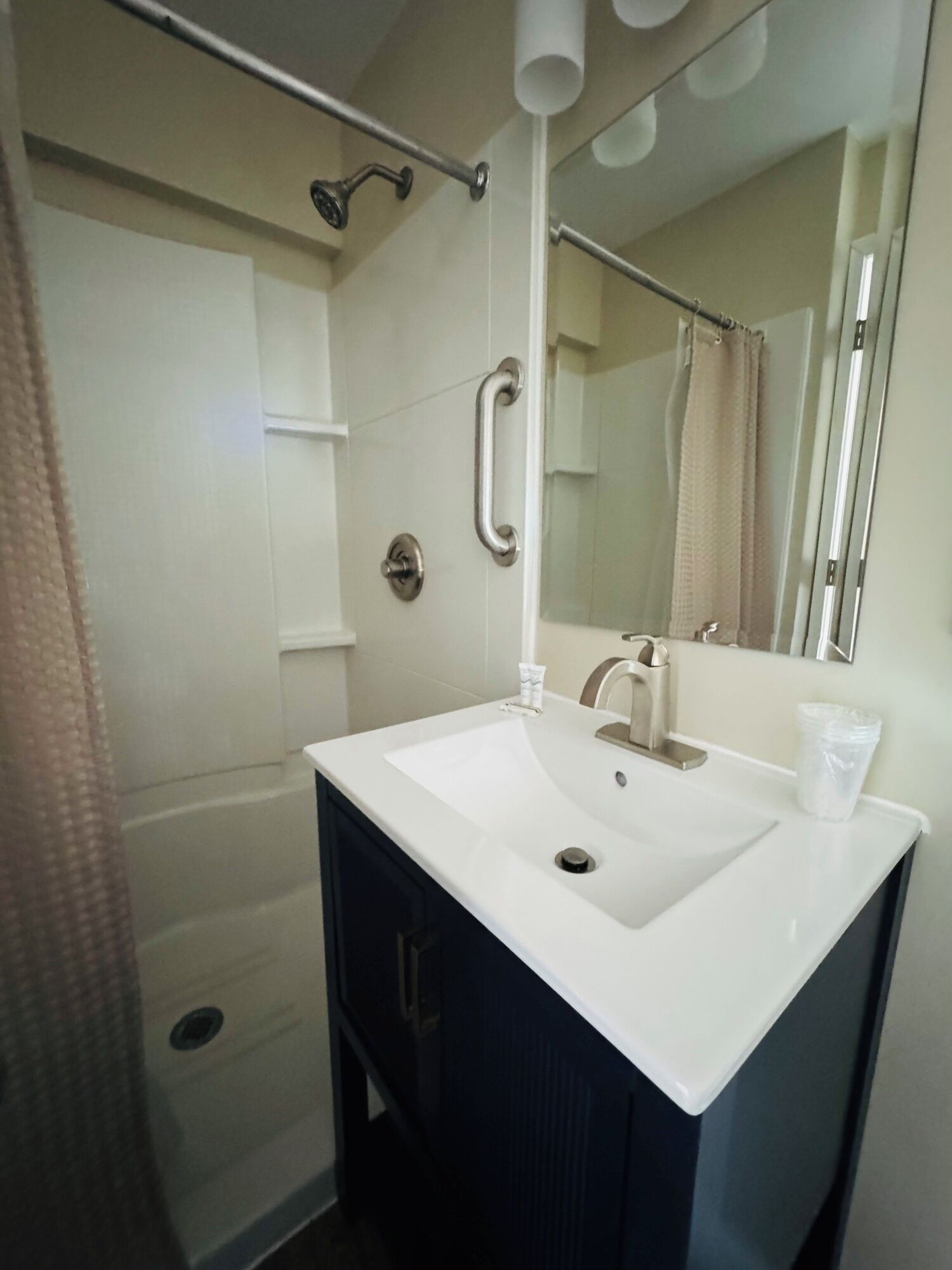 A bathroom with a white sink, a mirror, a shower, and a towel rack.