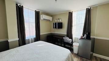 A hotel room with a bed, a desk, a TV, and a refrigerator.