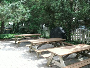 A picnic area with wooden tables and benches, surrounded by a wooden fence and greenery. - Unit 2 of 3: 3-bedroom apartment with AC in Seaside Park across from bay beach. (Seaside Park)