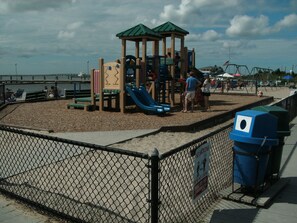 A playground with a slide and climbing structures, surrounded by a chain-link fence. - Unit 2 of 3: 3-bedroom apartment with AC in Seaside Park across from bay beach. (Seaside Park)