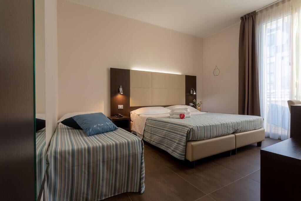 A hotel room with two beds, a large mirror, a nightstand, and a view of the outdoors.